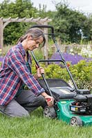 Woman adjusting the cutting height of a rotary lawn mower in long grass