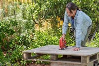 Woman using electric jigsaw to cut up a wooden pallet