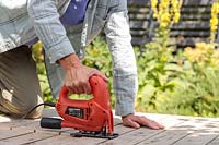 Woman using electric jigsaw to cut up a wooden pallet