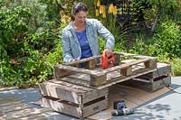 Woman using an electric jigsaw to cut a whole in the middle of a pallet