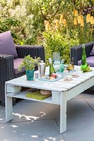 Outdoor chairs by wooden pallet table , with integral drinks cooler on slate patio in summer set up for a party.
