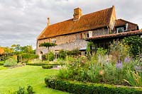 View of the house, and terrace from the barn. Plants include bronze fennel, Foeniculum vulgare 'Purpureum' and Perovskia atriplicifolia in the foreground and a standard, flat-topped crab-apple, Malus 'Sentinel', chosen to allow a view down the garden to the countryside from the house. Box edging contains the borders.