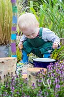 Young toddler playing with saucepan in sensory garden