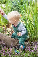 Young toddler climbing over a tree stump in sensory garden