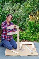 Woman inserting side panels for a raised planter being built from a kit
