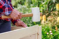 Close up detail of using a soft rubber mallet to insert wooden side panels into a pre-cut grove