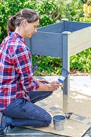 Woman painting a wooden raised planter with grey paint