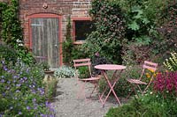 Pink metal table and chairs by brick potting shed in small paved courtyard.