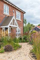 View to house across front garden laid out with beds featuring tall grasses and a winding brick path