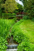 Stream flowing from lake with distant red bridge and waterfall beyond - Open Gardens Day, Nacton, Suffolk