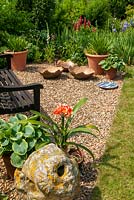 Garden seat on gravel with container grown Hostas and Amaryllis belladonna - Easter Lilly - and ornamental bowls - Open Gardens Day, Palgrave, Suffolk