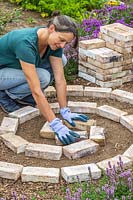 Woman wearing gloves placing bricks in a a spiral shape