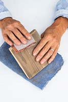 Woman using sandpaper to smooth the edges of the piece of timber which will be used as a shelf