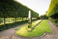 Stainless steel obelisk standing at the head of a water rill framed by hornbeam allee in June