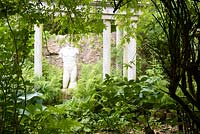 Classical statue framed by temple columns and lush planting including ferns and hostas in the walled garden 