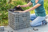 Woman folding over excess liner at the top of gabion basket lined with granite blocks and sand. 