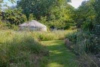 Wild flower meadow with mown path leading to yurt. 