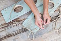 Woman tying knot in end of rope to prevent the wood shelves sliding off. 