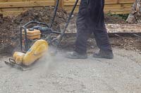 Man compressing foundation of crushed concrete for patio with compaction plate. 