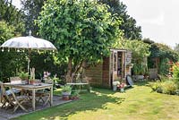 Wooden dining table and chairs with decorative parasol and view to garden and potting shed