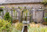 Courtyard garden with timber pergola, rill, galvanised trough water feature and planting including Stipa tenuissima, S. gigantea, Phlomis russeliana, irises and silvery stachys at Am Brook Meadow, Devon in August. 