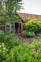 View across informal borders with rusted steel obelisk to circular paved area in front of studio