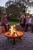 A lit firepit with people sitting on gabion benches 