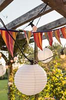 Detail of colourful bunting and lit chains of lights hanging from underside of wooden pergola