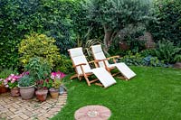 Small garden with artificial lawn and sun loungers, backed by mixed border and with small patio and containers nearby