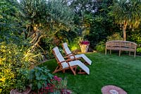 Small garden with artificial lawn and seating surrounded by mixed borders with garden lights 