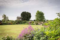 View across the main lawn towards lushly planted, colour-themed borders at Bourton House, Gloucestershire, UK.