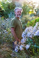 Nick Macer in the garden with Agapanthus 'Windsor Grey' in foreground, Pan Global Plants, Frampton on Severn, Gloucestershire, UK.
