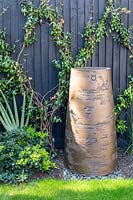 Large statement pot from Torc pots with metallic surface and evergreen climber Trachylospermum on wire trellis behind.