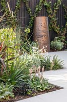 White zig zag paving with mixed planting and view to large pot in background. 