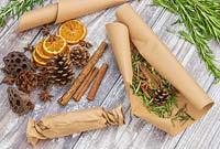 Scented fire starters made with Salvia rosmarinus syn. Rosmarinus - Rosemary - in brown paper with cinnamons sticks, orange slices, star anise and pine cones 