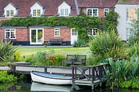 The 'gin and tonic boat' is moored on the pontoon, behind the house with its wisteria-covered wall. Planting includes Phormium tenax and Thalia dealbata.