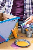 Woman using small roller to paint triangle sections on wooden box