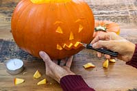 Woman carving halloween face into pumpkin with sharp kitchen knife