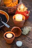 Table with various autumnal candle decorations, squashes, lichen, terracotta pots and black grit