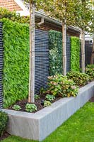 Stained grey wooden slatted fence with blocks of artificial plants and raised bed