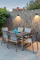 Modern dining furniture backed by slate covered wall and wall-mounted downlighters