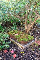 Finished hedgehog house made simply with bricks and a paving slab - camouflaged with wood chippings and moss