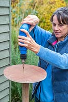 Woman using electic screwdriver to fix wooden disk to post