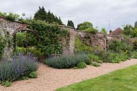 A serpentine or crinkle crankle wall with gated archway and gravel path and long border planted with nepeta, euphorbia and allium