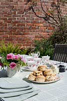 Outdoor table with laid out for a traditonal afternoon tea with roses in a jug