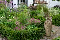 A yew-edged bed planted with hardy Geranium, Allium, Thalictrum and Agastache, empty urn and Taxus - Yew - ball topiary nearby