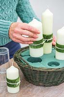 Woman adding the pillar candles to the precut holes in the oasis holding the candles firmly