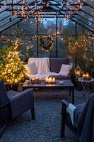 Lounge furniture inside greenhouse decorated for Christmas with tree, fairylights and candles