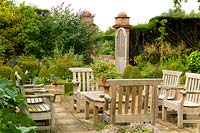 Teak furniture in a paved courtyard surrounded by a herbaceous borders at East Ruston Old Vicarage