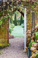 View through the Courtyard Garden gate to The Yew Walk at Wollerton Old Hall Garden, Shropshire - Planted above the gate is Clematis rehderiana